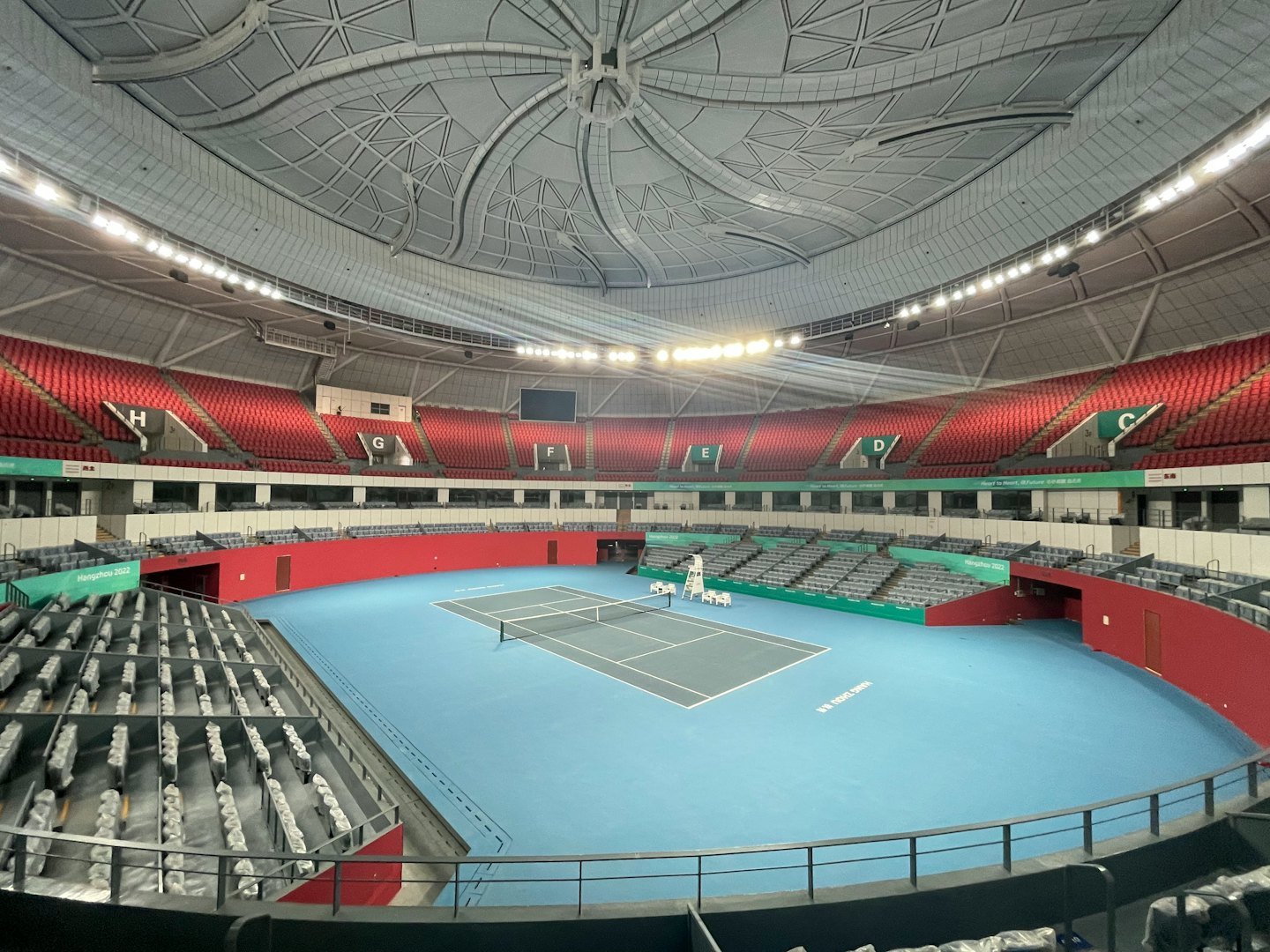 Empty tennis court sits inside a large indoor stadium arena.