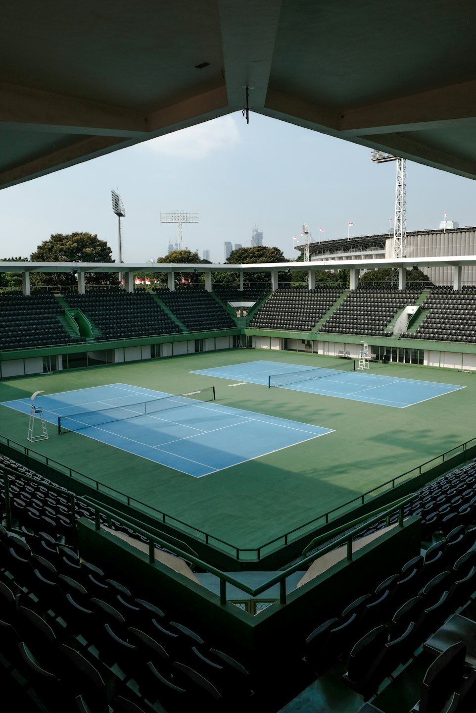 Empty tennis stadium courts surrounded by tiered green seating.