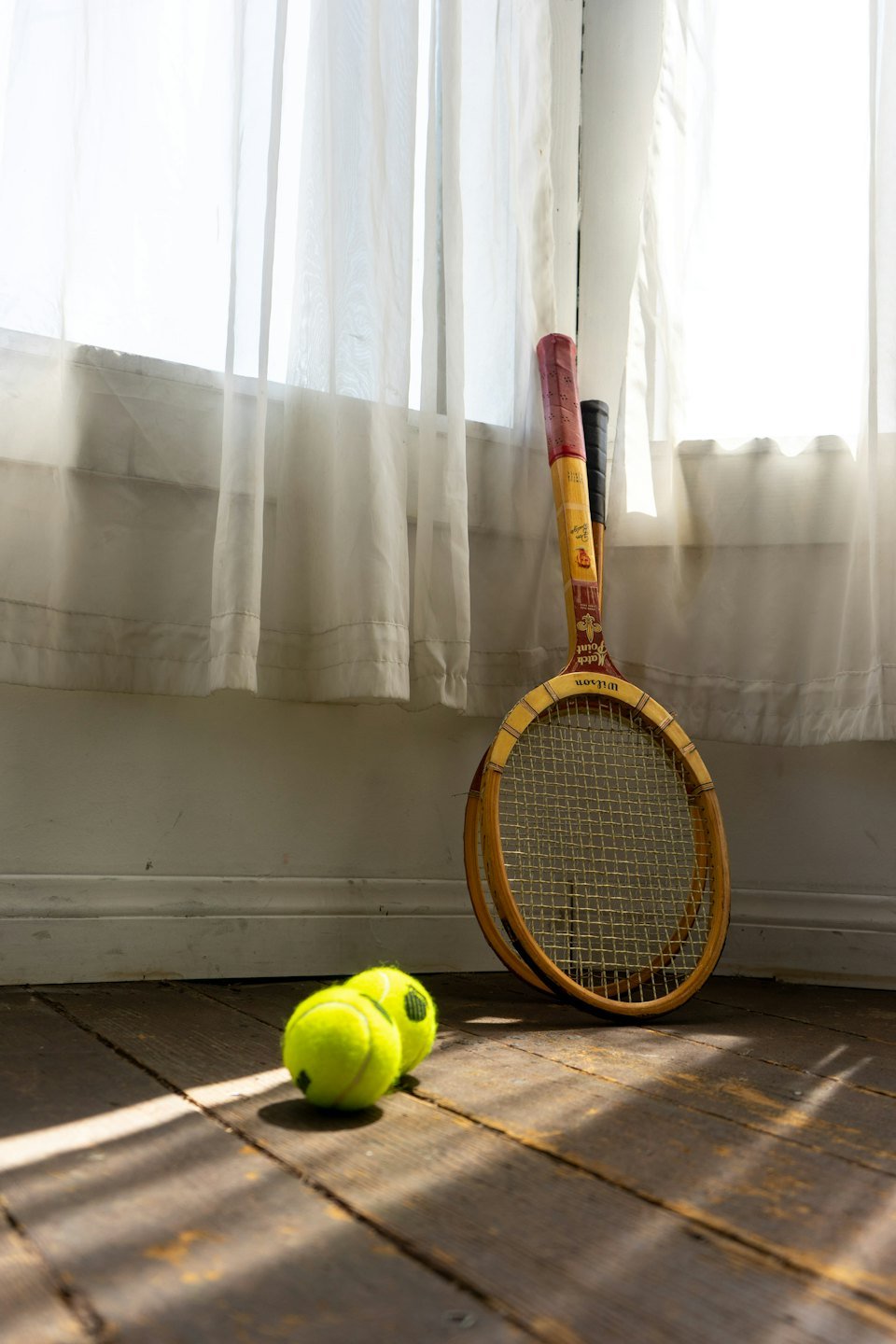 Two vintage wooden tennis rackets and balls on a floor.